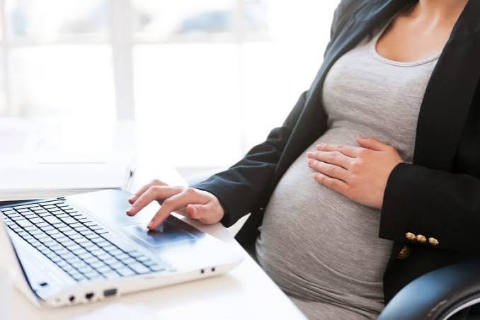 Mulher grávida trabalhando, com a mão sobre a barriga